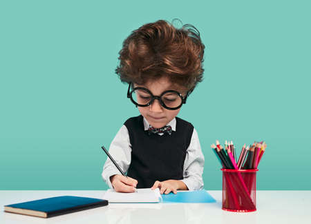 Focused cute schoolboy doing homework at tableの写真素材