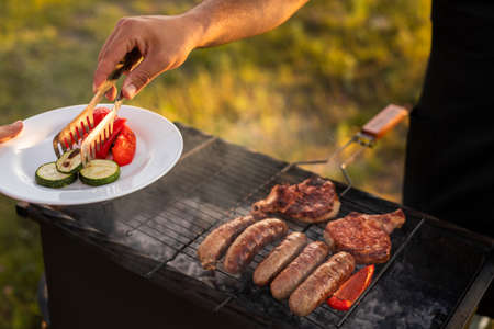 Crop person grilling vegetables and meat on outdoor barbecue oven