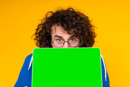Young guy covering mouth with netbook with green screenの写真素材