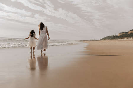 Anonymous female with little kid holding hands and walking on beachの写真素材