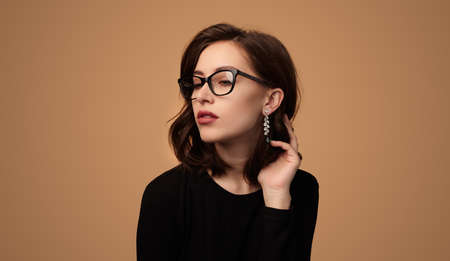 Stylish lady in glasses touching hair and looking away in studioの写真素材