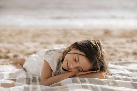 Smiling kid with closed eyes relaxing on sandy seashoreの写真素材