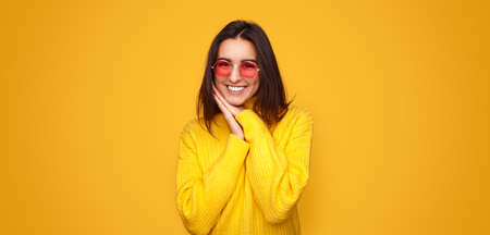 Excited stylish young ethnic woman smiling at camera in yellow studioの写真素材