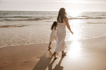 Mother and daughter walking near sea at sunriseの写真素材