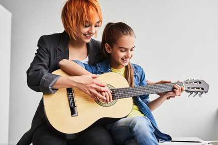 Cute child playing guitar during lesson with female teacherの写真素材