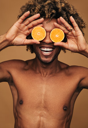 Merry black man playing with fresh orangeの写真素材