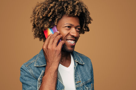 Cheerful black gay having phone call in brown studioの写真素材