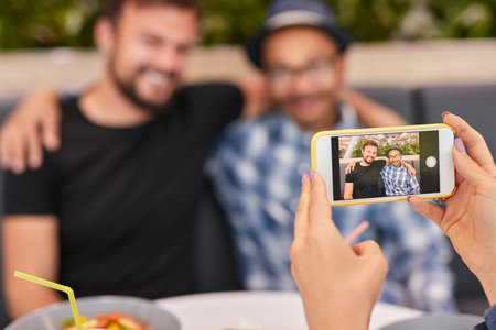 Crop lady photographing smiling diverse friends in cafeteria