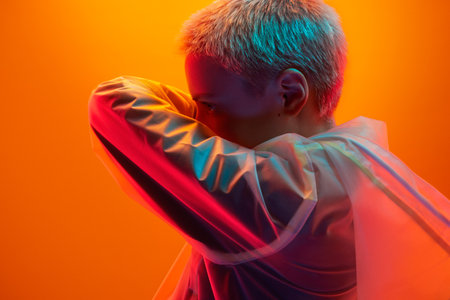 Attentive futuristic woman covering face with arm in orange studioの写真素材
