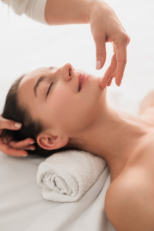 Unrecognizable masseuse doing facial treatment to calm happy female customerの写真素材