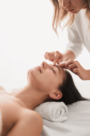Crop masseuse massaging face of client in spa salonの写真素材