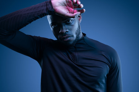 Tired black sportsman wiping sweat from forehead in studioの写真素材