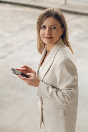 Young positive businesswoman browsing smartphone on streetの写真素材