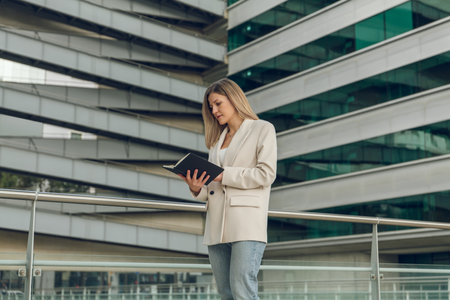 Focused young businesswoman checking schedule in notebook at office buildingの写真素材