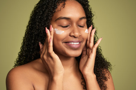 Smiling black woman applying cream on faceの写真素材