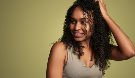 Smiling black woman touching curly hair in studioの写真素材