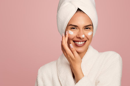 Cheerful woman applying cream on face after showerの写真素材