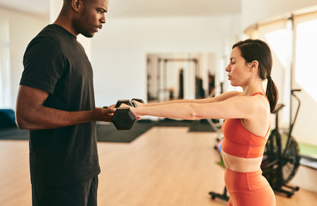Muscular black trainer helping sportswoman exercising with dumbbellsの写真素材