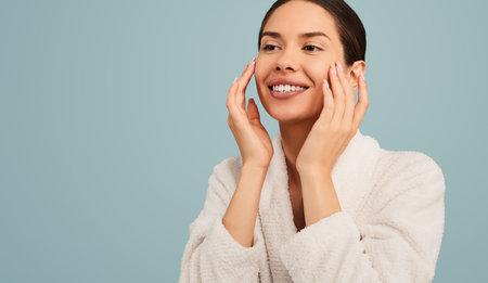 Happy young woman applying cosmetic product on faceの写真素材