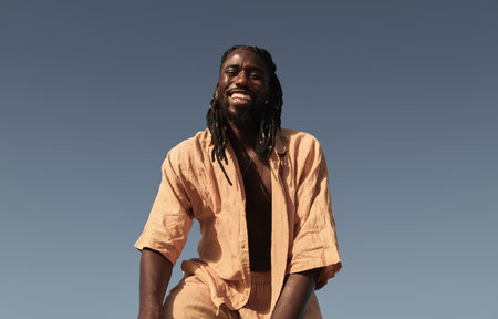 Cheerful black man with dreadlocks smiling against blue skyの写真素材