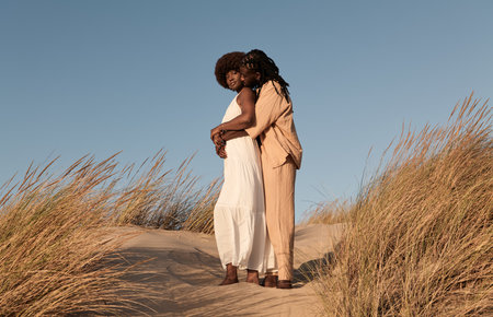 Black man embracing pregnant woman in fieldの写真素材