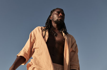 Young black man standing and looking away under blue skyの写真素材