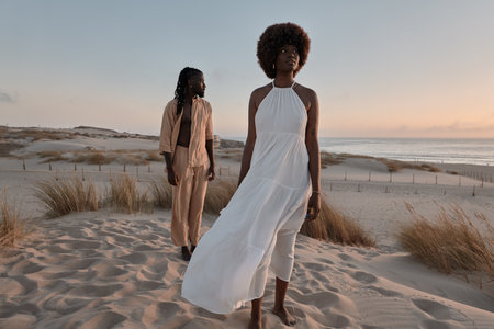 Black couple standing away on sand with dry grass plants in evening lightの写真素材