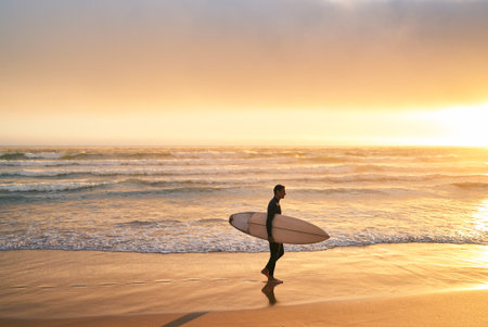 Surfer Walking Along Beautiful Beach at Sunset with Surfboard