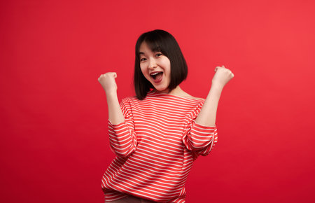 Excited Woman Celebrating Success Against Red Backgroundの写真素材