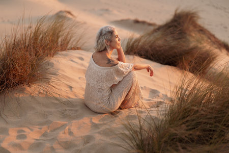 Woman Sitting on Sandy Dunes Reflecting During Golden Hour Sunsetの写真素材