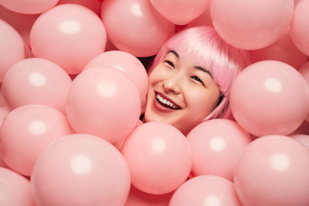 Smiling Woman Surrounded by Pink Balloons in Playful Settingの写真素材