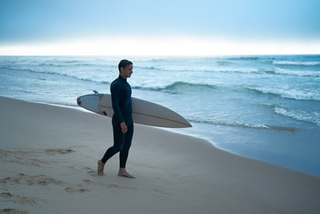 Surfer Walking on Beach with Surfboard During Dawnの写真素材