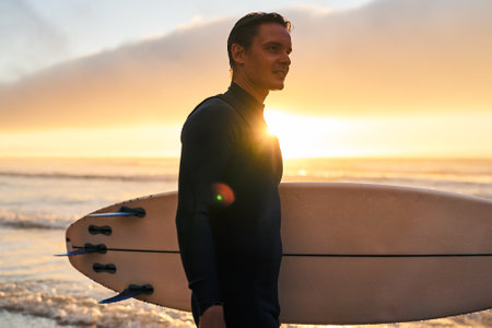 Surfer Holding Surfboard at Sunset on the Beachの写真素材