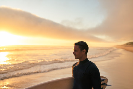 Surfer Standing on Beach at Sunset with Surfboard