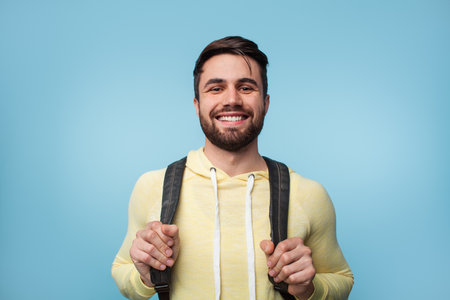 Smiling Man Wearing Yellow Hoodie and Backpack on Blue Backgroundの写真素材