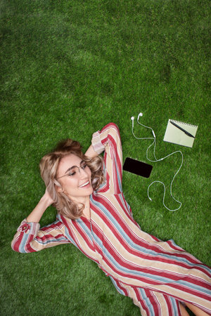 Relaxed Young Woman Lying on Grass With Accessories and Smileの写真素材