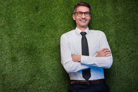 Confident Businessman Standing Against a Green Grass Wall in Formal Attireの写真素材