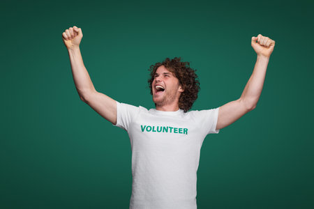 Happy Volunteer Celebrating Achievement with Raised Arms on Green Backgroundの写真素材