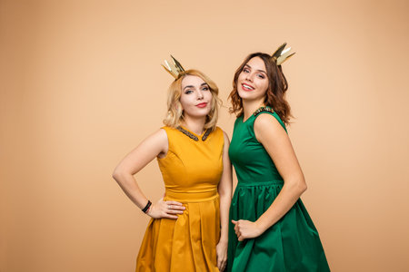 Two Stylish Women Posing in Elegant Dresses With Golden Crown Decorationsの写真素材