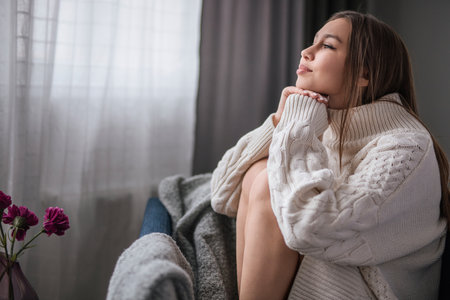 Woman in Cozy Sweater Relaxing by the Window with Bright Interior Lightの写真素材
