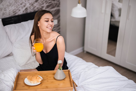Woman Enjoying Breakfast in Bed With Croissant and Orange Juiceの写真素材