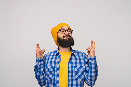 Excited Bearded Man Crossing Fingers and Smiling in Hopeful Anticipationの写真素材
