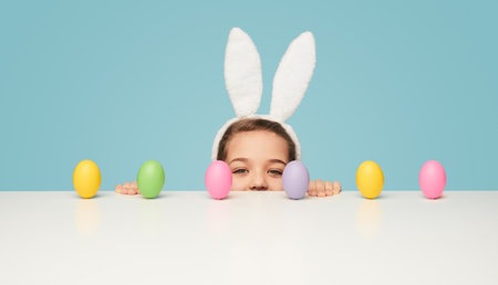 Girl with peeking out from behind table with Easter eggsの写真素材