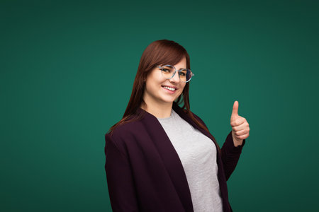 Smiling Woman in Glasses Giving Thumbs Up Against Green Backgroundの写真素材