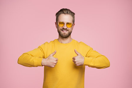 Happy Man in Yellow Sweater Giving Thumbs Up on Pink Backgroundの写真素材