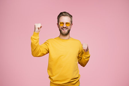 Excited Man in Yellow Sweater Celebrating on a Pink Backgroundの写真素材