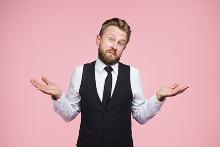 Confused Businessman in Formal Attire Shrugging Against a Pink Studio Backgroundの写真素材
