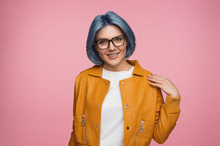 Stylish Woman with Blue Hair in Yellow Jacket Smiling on Pink Backgroundの写真素材