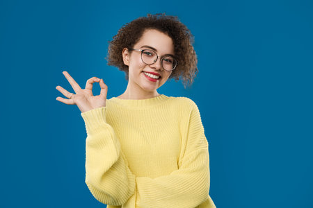 Woman in Yellow Sweater Showing OK Gesture with a Bright Smileの写真素材