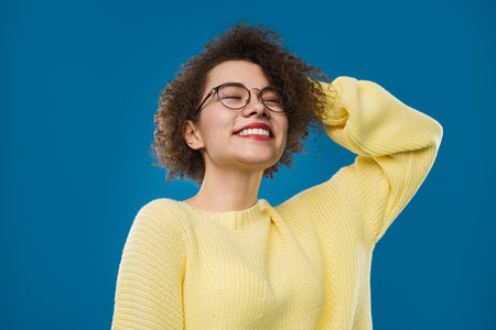 Smiling Young Woman in Yellow Sweater Against Vibrant Blue Backgroundの写真素材